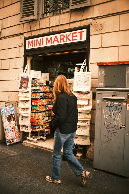 Woman walks past a mini market storefront.