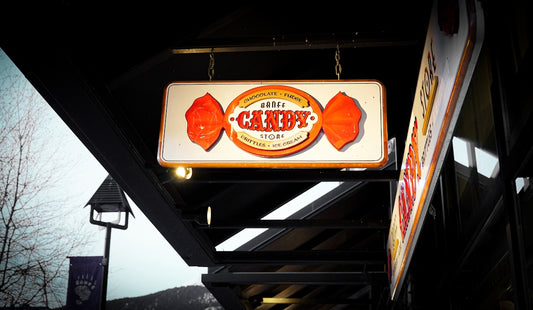 An illuminated candy store sign shaped like a wrapper.