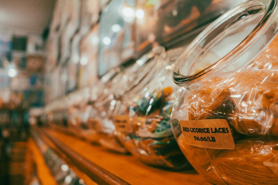Candy jars, including red licorice, displayed on a wooden shelf.