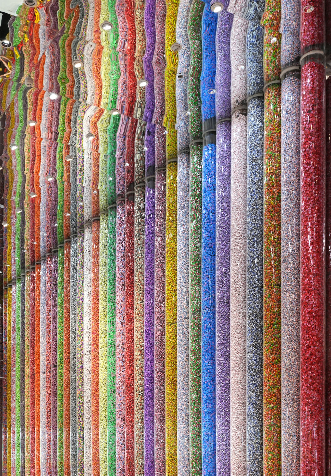 Vertical clear tubes filled with colorful candies reflected in a mirrored ceiling