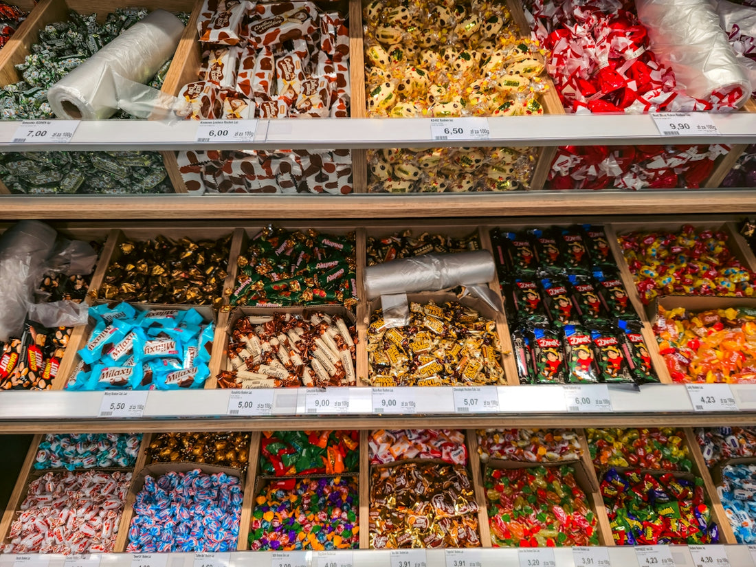 Assorted wrapped candies in wooden bins on supermarket shelves with price tags
